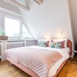 Schlafzimmer mit Dachschrägen, großem Fenster und Bett mit rosa Bezügen.