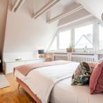Schlafzimmer mit Dachschrägen, Bett, Sofa und Fenster mit Blick auf Dächer.