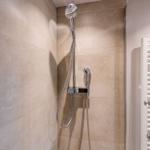 Dusche mit Handbrause und Duschwand aus hellen Fliesen.