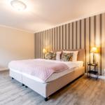 Schlafzimmer mit Bett, Streifenwand und Nachttischen.