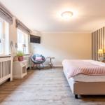 Schlafzimmer mit Bett, Fenstern, Stuhl und Wandbehang.