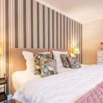 Schlafzimmer mit Bett, Kissen, Nachttisch und Schrank. Wand mit Streifen tapete.