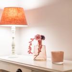 Weißer Nachttisch mit Lampe, Vasen und Kerze.