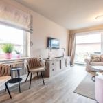 Wohnzimmer mit Sofa, Sitzgelegenheiten und TV. Große Fenster und Licht.