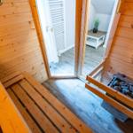 Sauna mit Holzbank und Steinofen. Durchgang zu einem Raum mit Heizkörper.