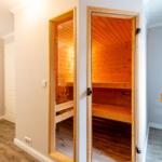 Sauna mit Holzbank und warmem Licht. Tür offen, Blick ins Innere.