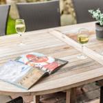 Holztisch mit zwei Weingläsern, Zeitschrift und Pflanze im Freien.
