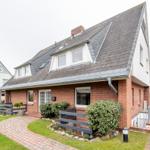 Ein zweistöckiges Haus mit rotem Backstein und grauem Dach, umgeben von Grünflächen und einem gepflasterten Weg.