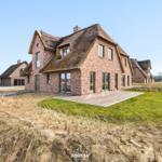 Moderne Ferienhaus mit Strohdach und Holzterrasse in ländlicher Umgebung.
