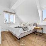 Schlafzimmer mit Dachschrägen, Bett, TV und Sessel.