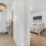 Badezimmer mit Waschbecken und Toilette. Nebenraum mit Bett und Wandbild.
