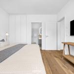 Schlafzimmer mit Bett, TV und Holzboden. Anschlussraum mit Bad und Dusche.