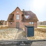 Haus mit strohgedecktem Dach und Steinmauer, gepflasterter Vorplatz