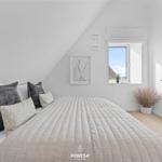 Bedroom with sloped ceiling, bed, window, and adjacent bathroom.