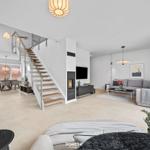 Living area with sofa, TV, and fireplace. Stairs lead to dining room with table and chairs.