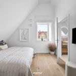 Schlafzimmer mit Dachschräge, Bett, Fenster und angrenzender Badewanne.