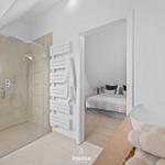 Badezimmer mit Dusche und Waschbecken. Schlafzimmer mit Bett im Hintergrund.