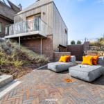 Terrace with gray lounge cushions and orange pillows. Background: modern house with wooden facade.