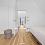 Bedroom with bed, wardrobe, and wooden floor. Corridor to living area.