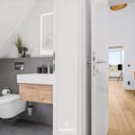 Bathroom with toilet and sink. View into living area with wooden floor and orange chair.