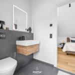 Bathroom with sink, mirror, and toilet. Bedroom with bed and wooden floor visible.