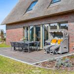 Deck with dining table, chairs, and beach chair in front of a thatched roof house.