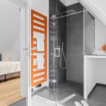 Bedroom with sloped ceiling and shower with orange towel rack.