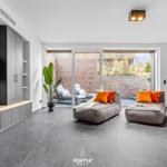 Living area with two gray chaises, orange cushions, and glass doors to terrace.