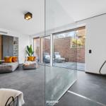 Modern living area with glass wall, loungers, and TV wall. Shower with shower head.