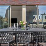 Terrace with dining table and chairs, view into the interior with fireplace.