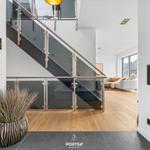 Modern staircase with glass railing leads to living area with sofa and wooden floor.