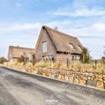 Modern villa with thatched roof and stone wall along the road.