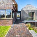 Modern villa with wooden and brick house, glass balcony, and paved path.