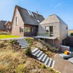 Modern villa with wooden and brick facade, terrace, and garden with dune view.