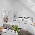 Bedroom with sloped ceiling, bed, nightstand, and view into bathroom.