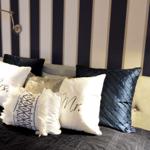 Headboard with pillows and wall lamps against striped wall.