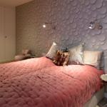 Bedroom with patterned wall, bed with pillows, and nightstand with seahorse decoration.