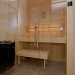 Sauna with wooden bench, glass wall, and heater.