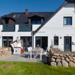 White villa with terrace, table and chairs, surrounded by stone walls and grass.