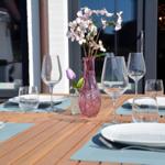 Set table with plates, glasses, and flowers on terrace.