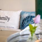 Sofa with cushions, one reading family, beside flower and candle.