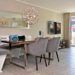 Dining area with glass table, gray chairs, and sofa with cushions. Hanging lamp and mirror on the wall.