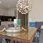 Dining area with glass top and gray corner sofa. Pendant light above table.
