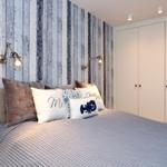 Bedroom with bed, pillows, and wooden wall paneling. White wardrobe and wall lamps.