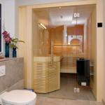 Sauna with glass wall, wooden bench, and heater in bathroom