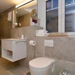 Bathroom with shower, sink and toilet. Window with flowers and towel stack.