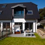 House with terrace, garden, and beach chair. Black roof, white walls, and wooden bench.