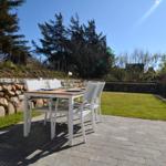 Patio with table and chairs, green lawn and stone wall in background.