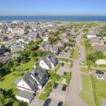 Aerial view of a coastal village with houses, gardens, and the sea in the background.