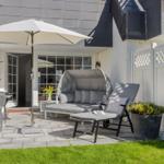 Terrace with seating, umbrella, and plants. Background: house with windows and white doors.